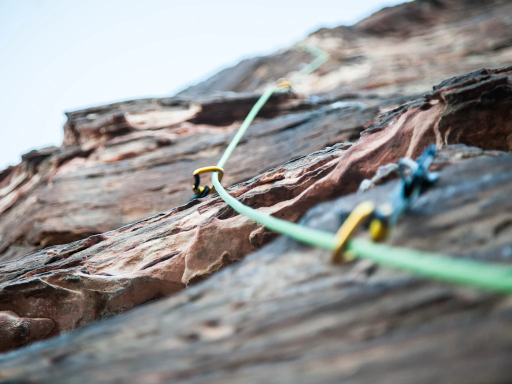 Corde d'escalade verte passant dans des dégaines sur une paroi rocheuse