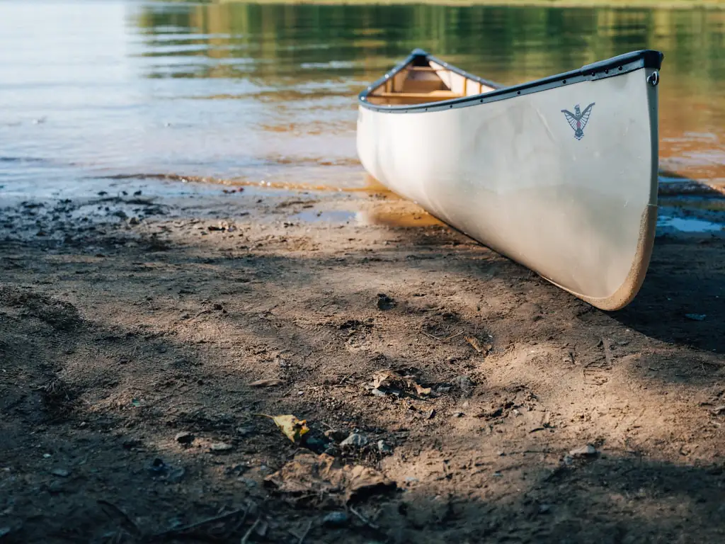 Canoë blanc posé sur la berge sablonneuse d'un lac
