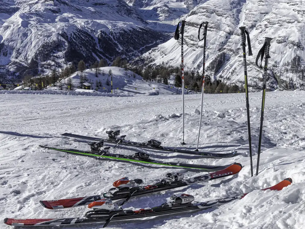Skis et bâtons posés dans la neige devant un versant enneigé